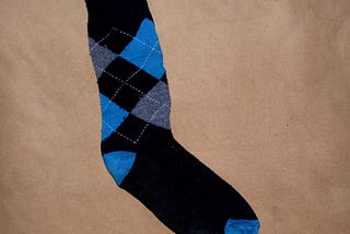 A black sock with a blue and grey Argyle pattern.