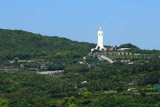 Large white Kannon statue in Japan on a hillside in the distance