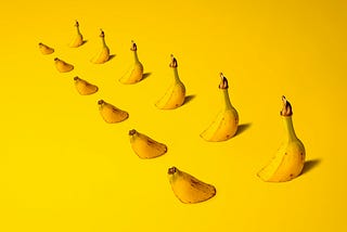 A row of bananas that have been cut and placed to look like they disappear through the surface on which they sit are place in a row, set against a yellow background. Representing the insights of Ramneek Bhoagl on the integration of chiropractic care and functional medicine.