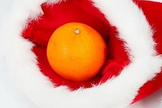 A large orange sits inside a red Christmas stocking with furry white trim.