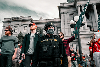 A picture of Trump supporters behind a cop, in front of a government building at a rally