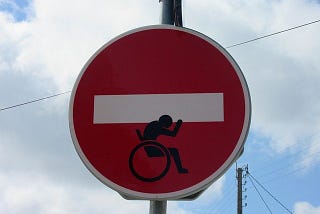 A No Entry sign with the white bar being carried by a wheelchair user