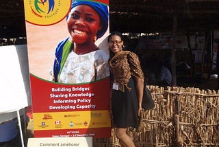 Dr Juliet Iwelunmor stands beside a banner for public health