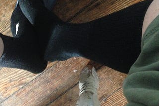 photo of two legs; short black sock on the left, longer one on the right