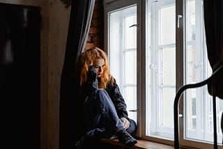 Woman sitting on a window bench, looking stressed and forlorn.