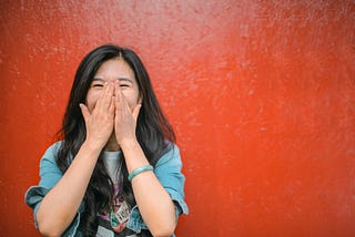 image: cheerful woman smiling in front of a bright orange wall