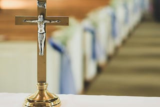 A small crucifix sitting on the altar of a church with a few empty pews in view.