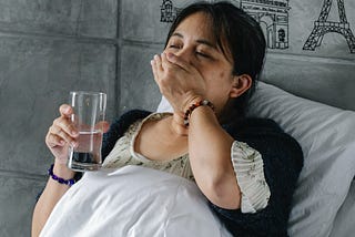 a woman laying on a bed while swallowing a pill and holding a glass of water