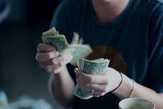 A person holding money on the left hand and counting it on the right hand for paying the bills.