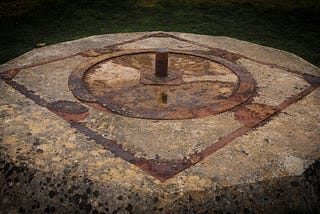 Moody photograph of a strange object resembling a ritual site, comprised of rusting metal embedded in concrete.