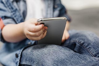Criança branca segurando um celular no colo.