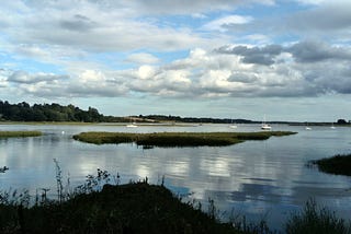 A calm estuary with boats, and fluffy grey clouds in the sky