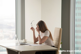 woman at her desk overworked and tired in front of a laptop