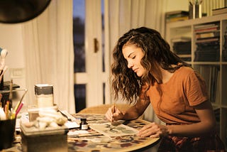 A woman sitting at a table painting with a small brush.