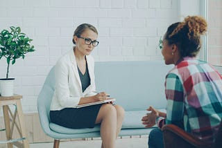 Psychiatrist taking notes during an in-person therapy session with a patient in a bright, modern office. Photo by Vitaly Gariev on Unsplash