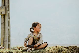 Lost young child pondering life, while sitting on the grass.