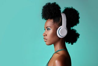 A woman listening to headphones in front of a teal wall.