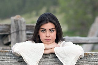 Woman leaning on the top of a fence looking at the camera