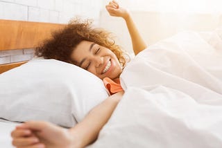 Happy girl lying in bed doing a morning stretch.