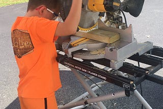 An eight-year-old boy working with a power chop saw as part of summer school.