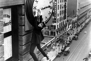 Silent film star Harold Lloyd hangs from a giant clock on the side of a building.