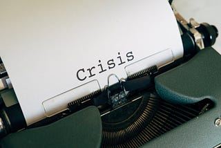 Antique typewriter sitting on a desk with one word written in bold on it: Crisis