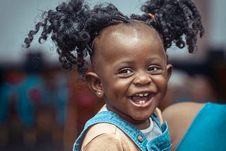 A child smiling at the camera. You can see all five of her milk teeth.