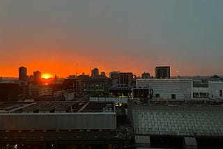 An orange sun rises over building rooftops in London.