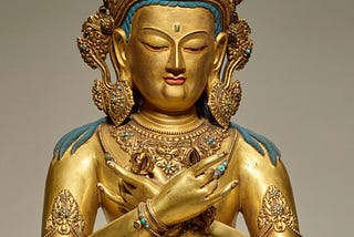 A golden figure of a Buddha, with a large golden crown, hands crossed on its chest.