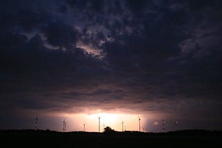 A dark sky at night lit up by a bright lightning strike.