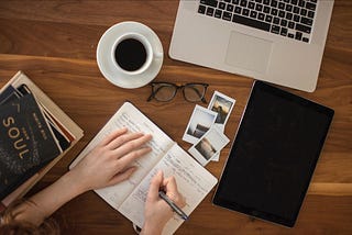 A person working at their computer with a notebook and a cup of coffee.