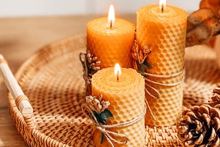 3 lit beeswax candles on a tray with a pine cone