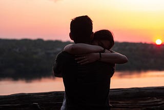 Girl hugs boyfriend tightly around his neck as the sun sets