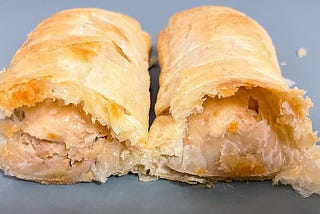 A close‑up of a Greggs meat‑free sausage roll cut in half, showing flaky golden puff pastry and a light, even plant‑based filling.