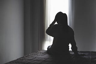 a woman wiht her back to a window. We can see her shadow and her hand is on her head. She looks sad. grief, family