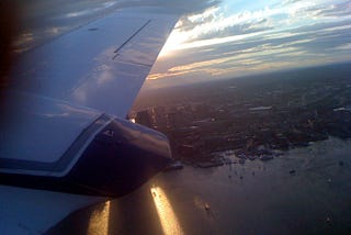 A small 10-seater plane overlooking Boston Logan Airport at sunset.