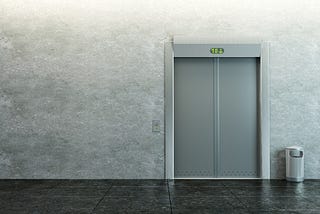The closed door of an elevator against a grey wall