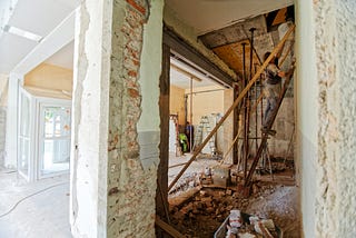 A room in a house mid-restoration, one half is painted but unfinished, the other is still partially rubble and wires