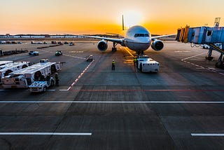 An aircraft sitting idle on the tarmac, in front of a deep, orange sunset.