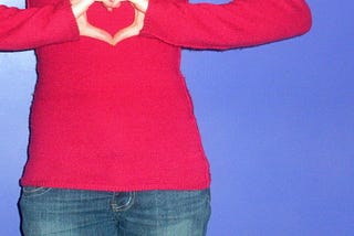 A woman holds her hands in the shape of a heart in front of her chest.
