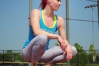 The author crouches down on a red track surface. Her arms are resting casually on her grey leggings and she is looking out over the track in thought.