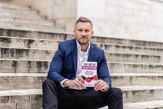 Tim Castle sitting on steps holding a copy of The Art of Negotiation