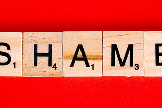 Scrabble tiles spell out the word “Shame” on a red background.