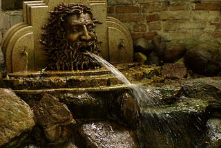 A fountain with a demonheaded figure shooting a stream of water out of its mouth onto the rocks below