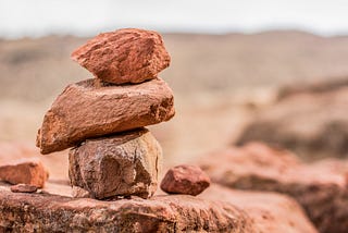 Three red rocks stacked on top of one another in a desert enviroment.