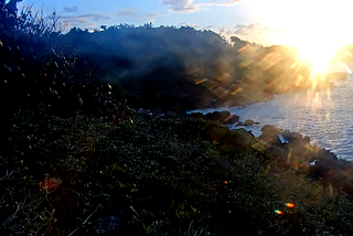 green wooded hills and rocky ocean beach with brilliant rising sun