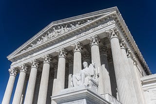 The United States Supreme Court building is photographed from below, showcasing its Greek architecture.