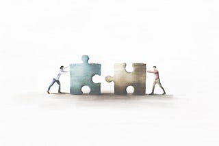Two people pushing two puzzle pieces that fit together towards each other.