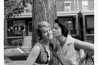 A woman kissing her sister in front of a tree in Bethesda, MD