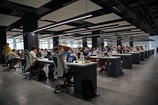 Workers sitting at their desks in a large office. One worker has his hands clasped behind his head.